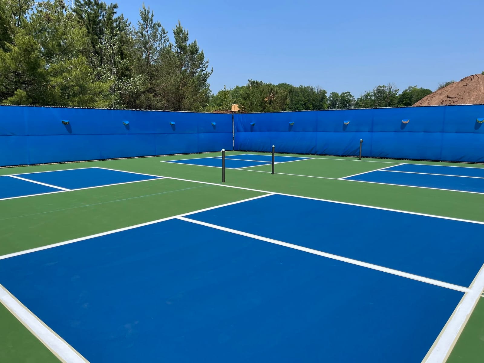 Four blue-and-green outdoor pickleball courts with permanent nets and windscreens at Art Ohlgren Recreational Area